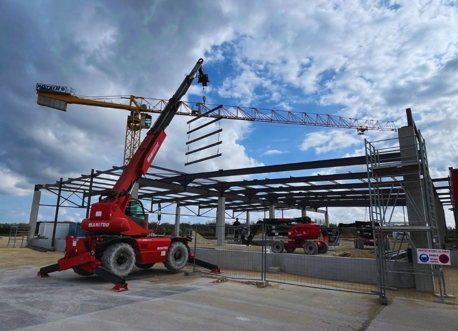 Grue rouge en action sur chantier, montage de charpente métallique en cours.