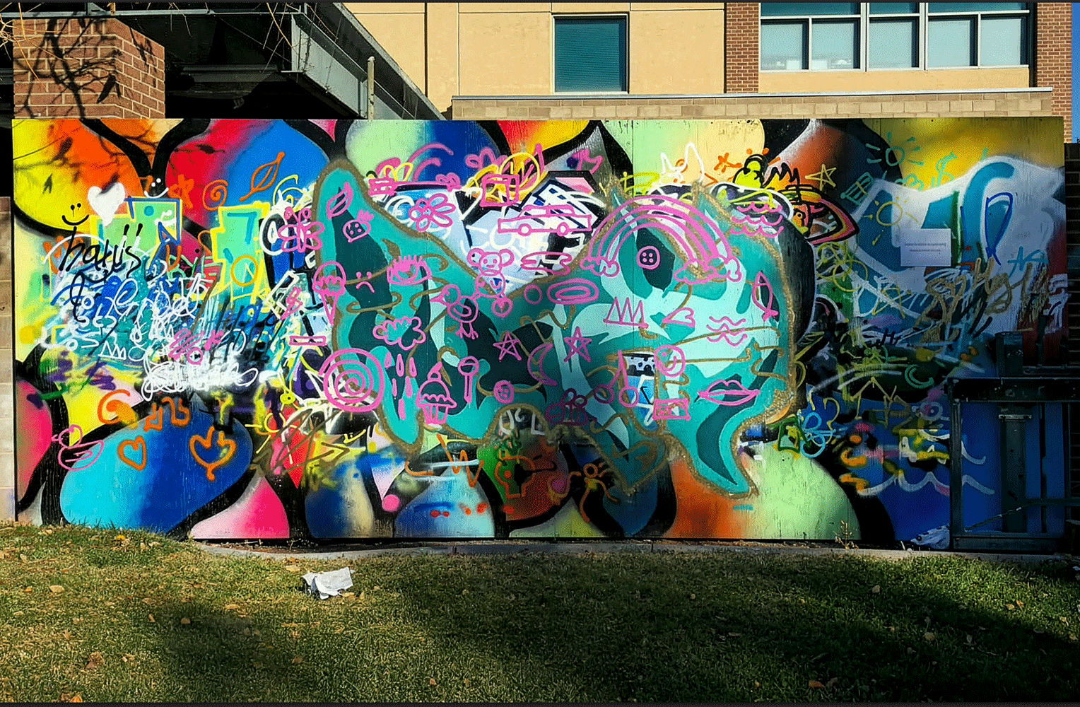 Colorful street art mural featuring abstract patterns and shapes in vibrant hues. Green grass in the foreground.