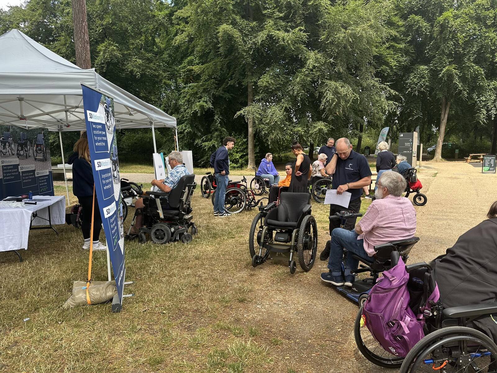 An outdoor gathering in the woods with visitors viewing wheelchairs at our gazebo