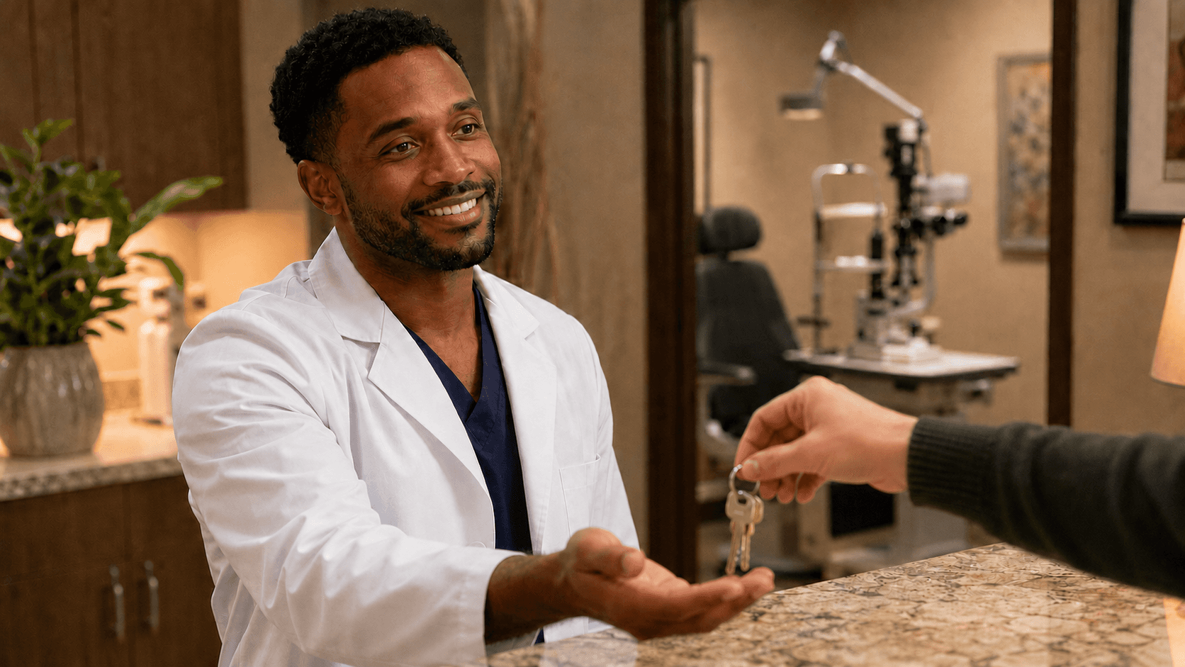 Young Black male ophthalmologist in a white coat smiling as he receives a set of keys at a practice reception counter, with a slit lamp blurred in the warm background