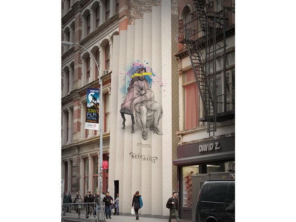 A mural of a seated figure with long hair and a beard, wearing a robe and holding a pillow, is painted on the side of a light-colored building. The figure is seated on a bench-like structure. Above the figure, colorful splashes of paint are visible. Below the figure, the name “KEVE ALLI” is painted. The building is part of a street scene, with pedestrians walking on the sidewalk and a streetlight visible to the left. A black van is parked on the street to the right of the building. A banner advertising a film festival is mounted on a nearby building.