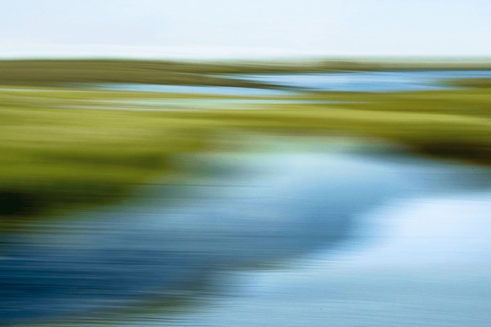 Woman smiling while seated at a desk with a laptop as a man in glasses leans over to show her something on the screen.