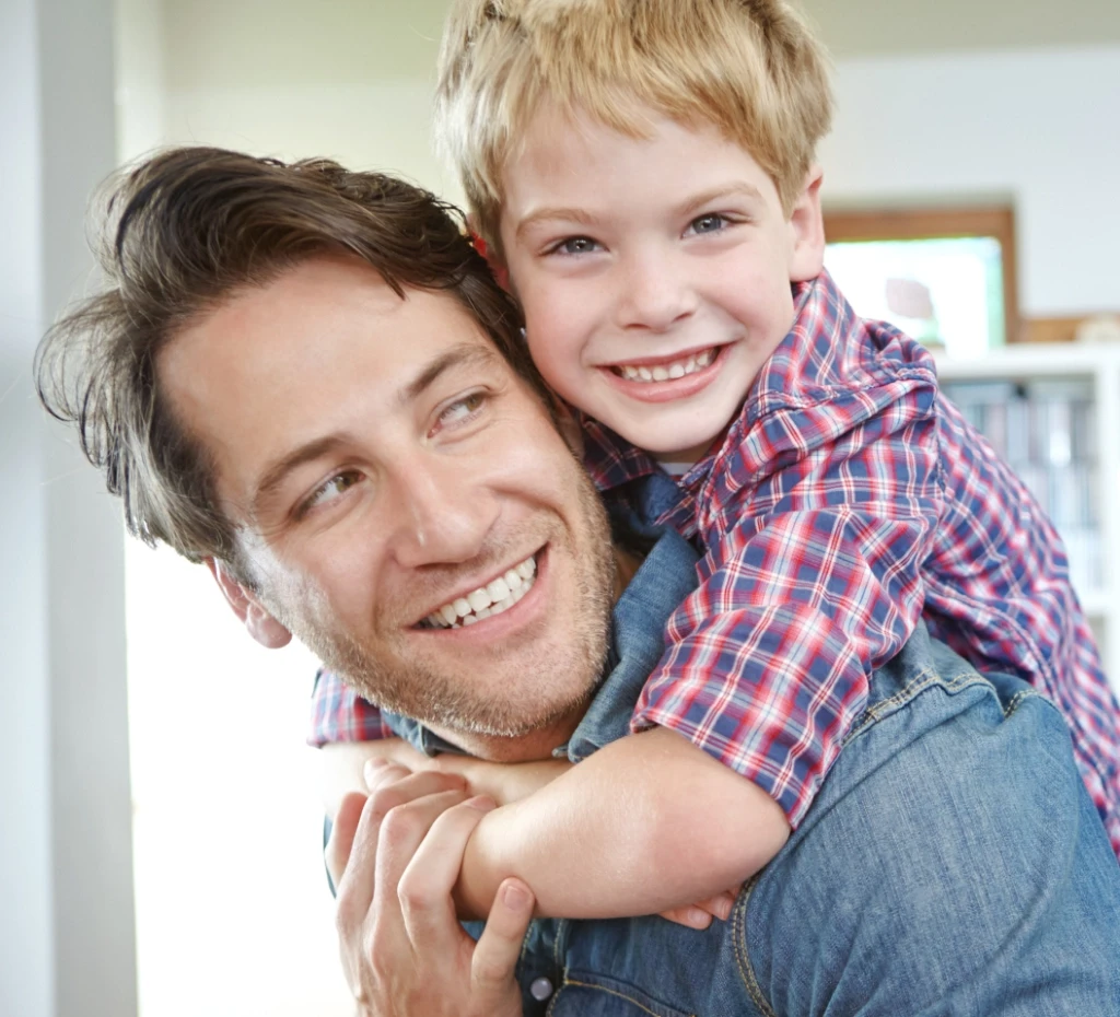 Smiling father with with smiling son hanging on his back.