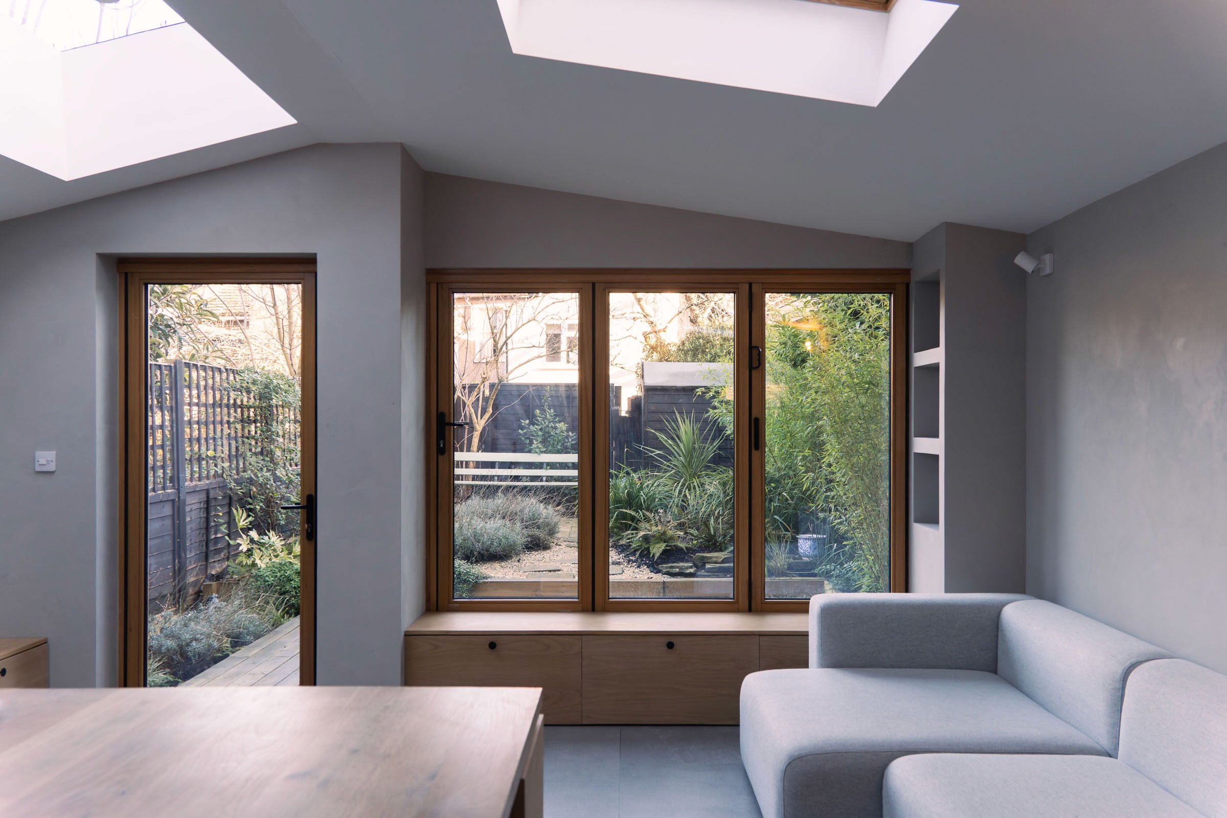 Architect-designed living room with grey sofa, timber window seat and glazed doors to garden, rear extension Brockley London — Alec Crisp Architects