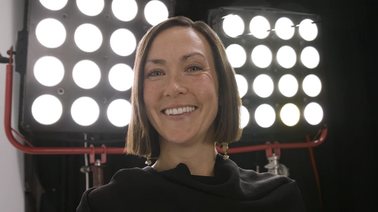 Sara Frasca on set during a video shoot, framed by two large LED lighting panels.