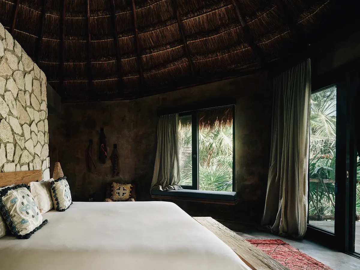 Arena Room at Nômade Tulum with beautiful jungle view through 2 huge windows, showing pillows and rug.