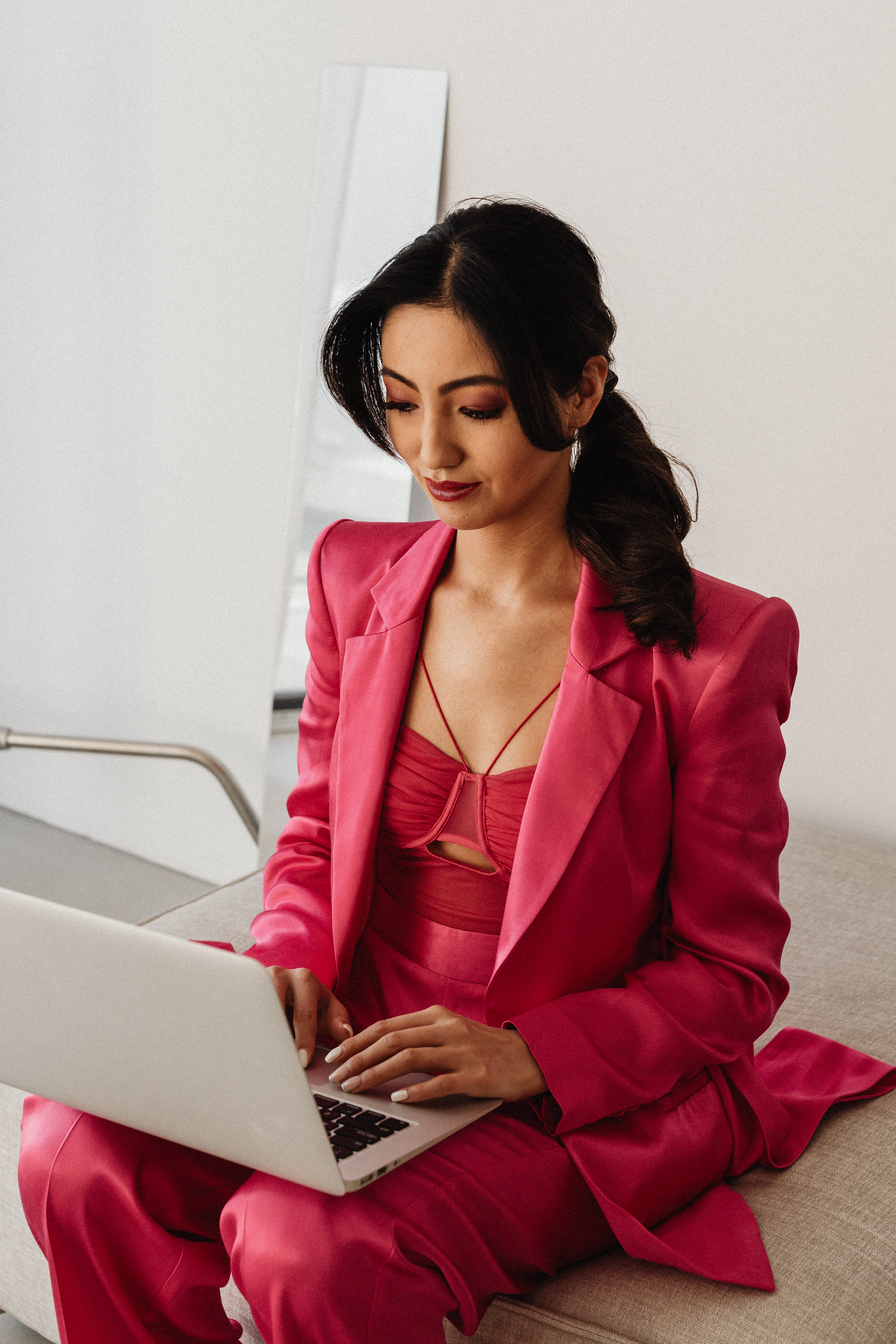 A focused woman sits and types on a laptop in a bright, minimalist room.