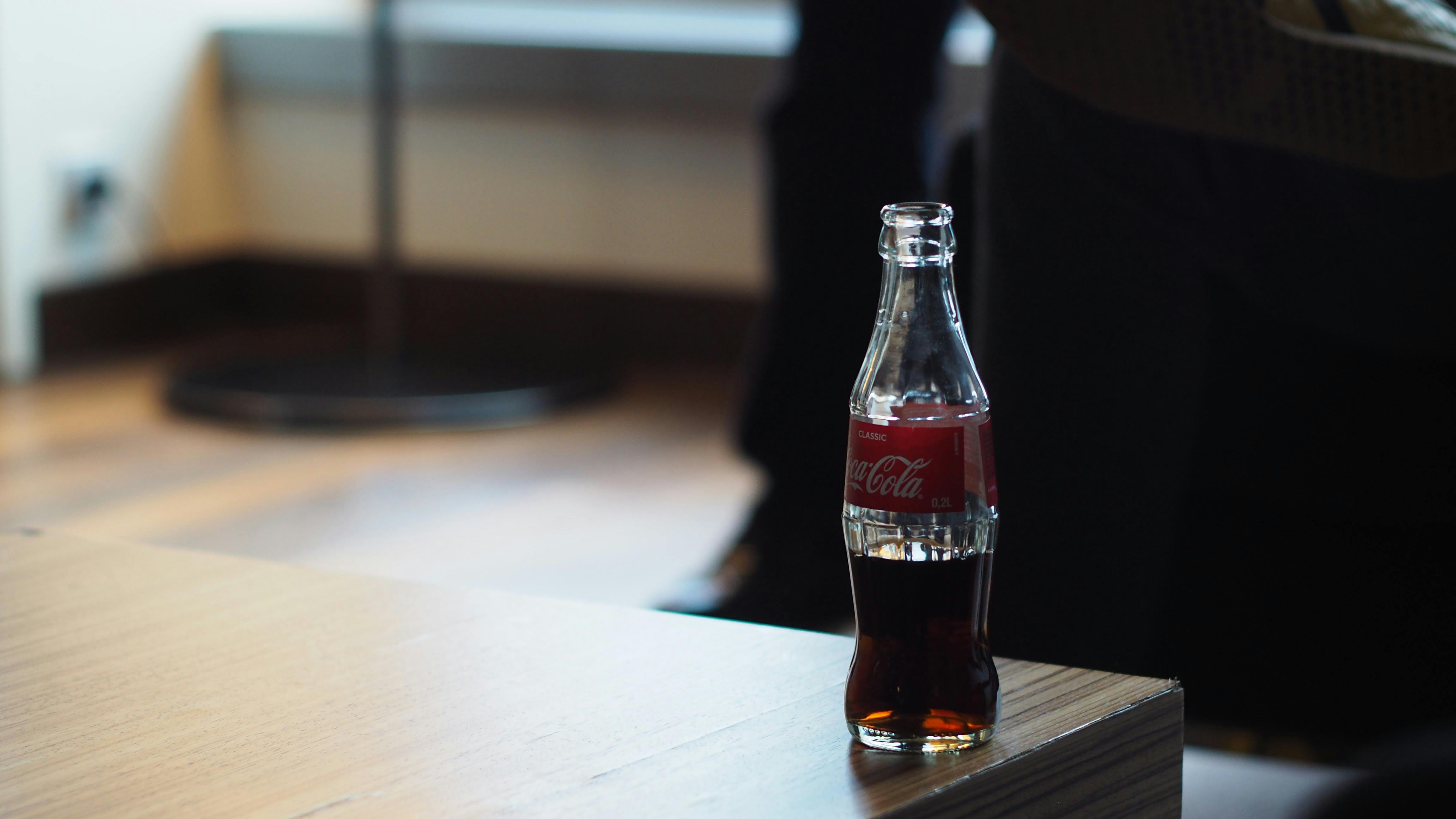 Glass bottle of Coca-Cola on a wooden surface.