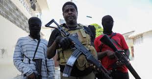 Jimmy Cherizier holds a gun. Two men wearing face masks are on his right and left side. Both men are holding guns.
