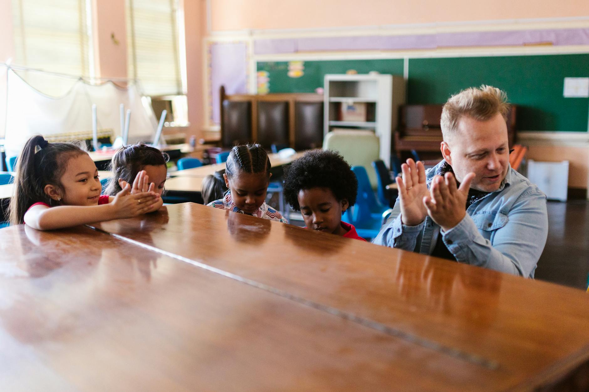 A teacher standing at a whiteboard raising a hand to lead classroom management games for quick student attention.