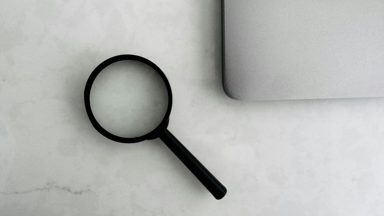 Vergrootglas naast een laptop op een marmeren tafel, symbool voor het onderzoeken van zoekresultaten