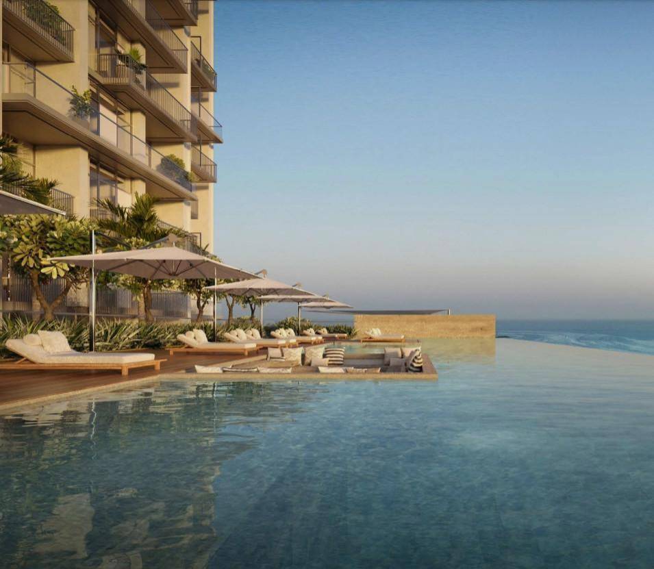 A picturesque scene featuring a pool and palm trees adjacent to the ocean, highlighting ARIA by Beyond's coastal charm.