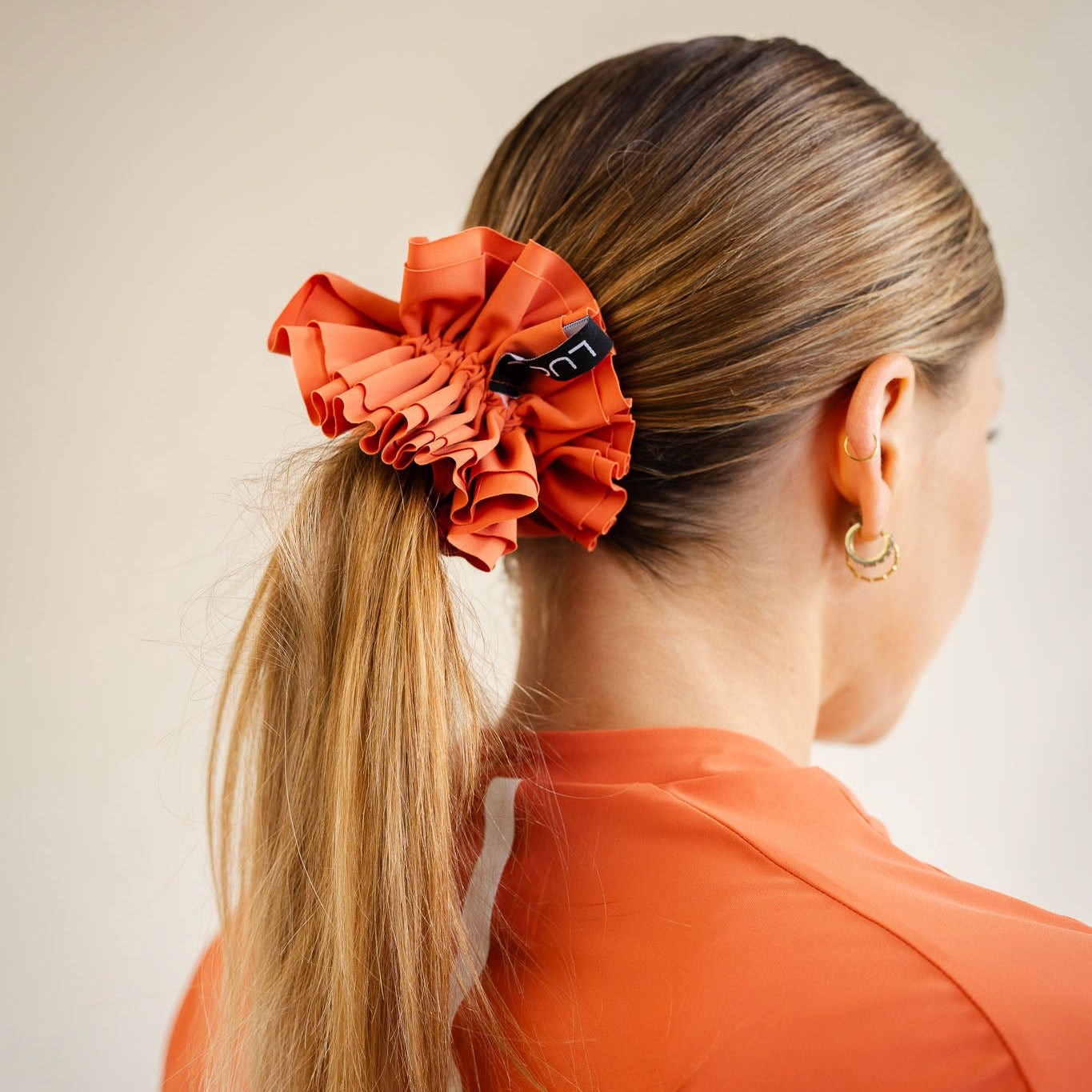Cyclist wearing LUCA Uplift scrunchie in aperol holding a ponytail, back view