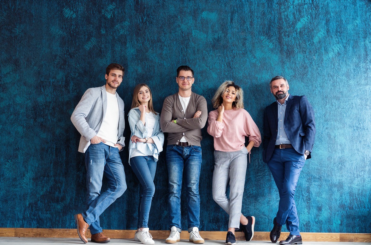 A diverse group of professionals standing against a blue wall, representing the inviting and inclusive culture at Inway Risk Management’s careers page.