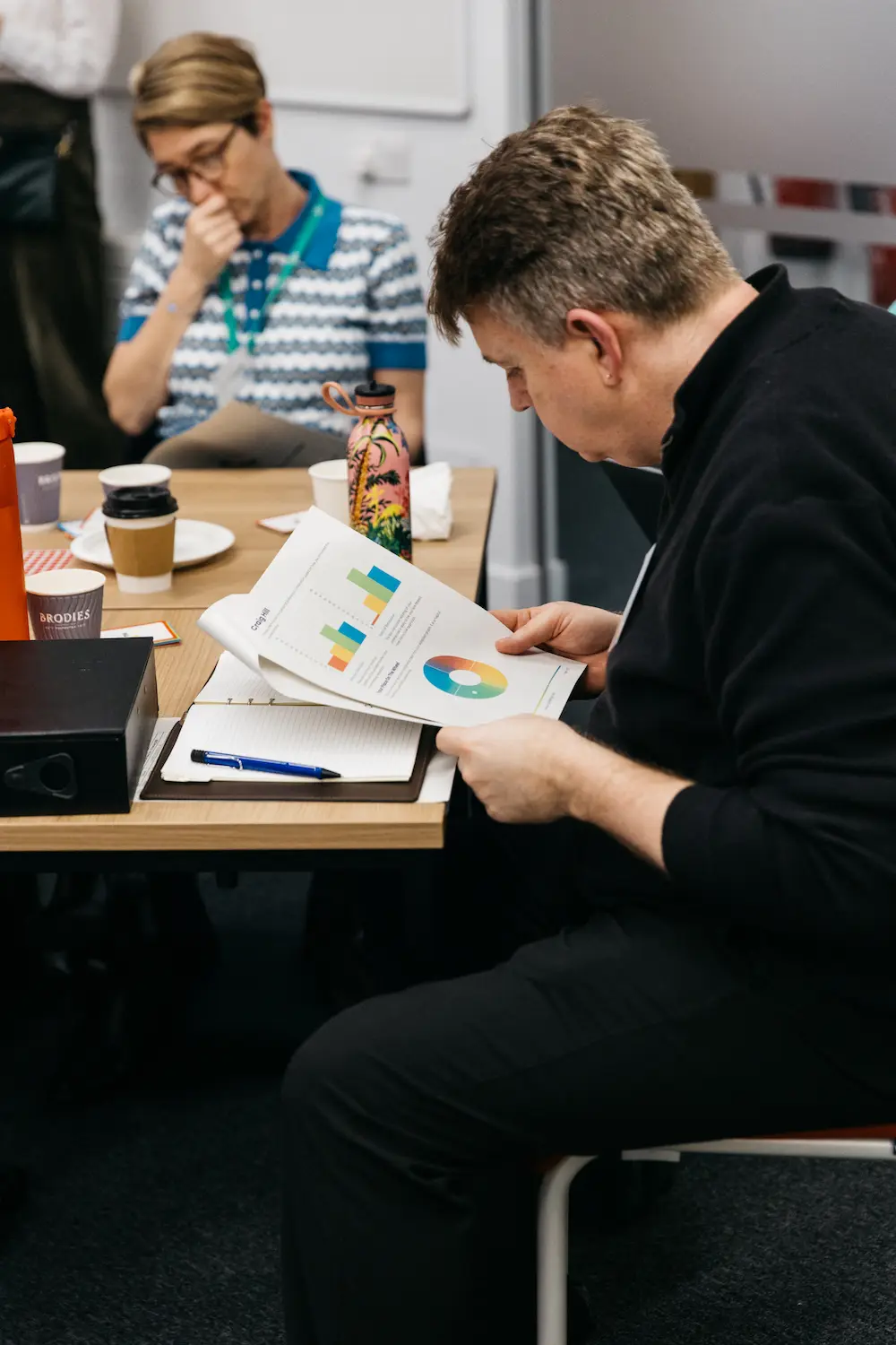 Person sitting at a table writing and making phone call.
