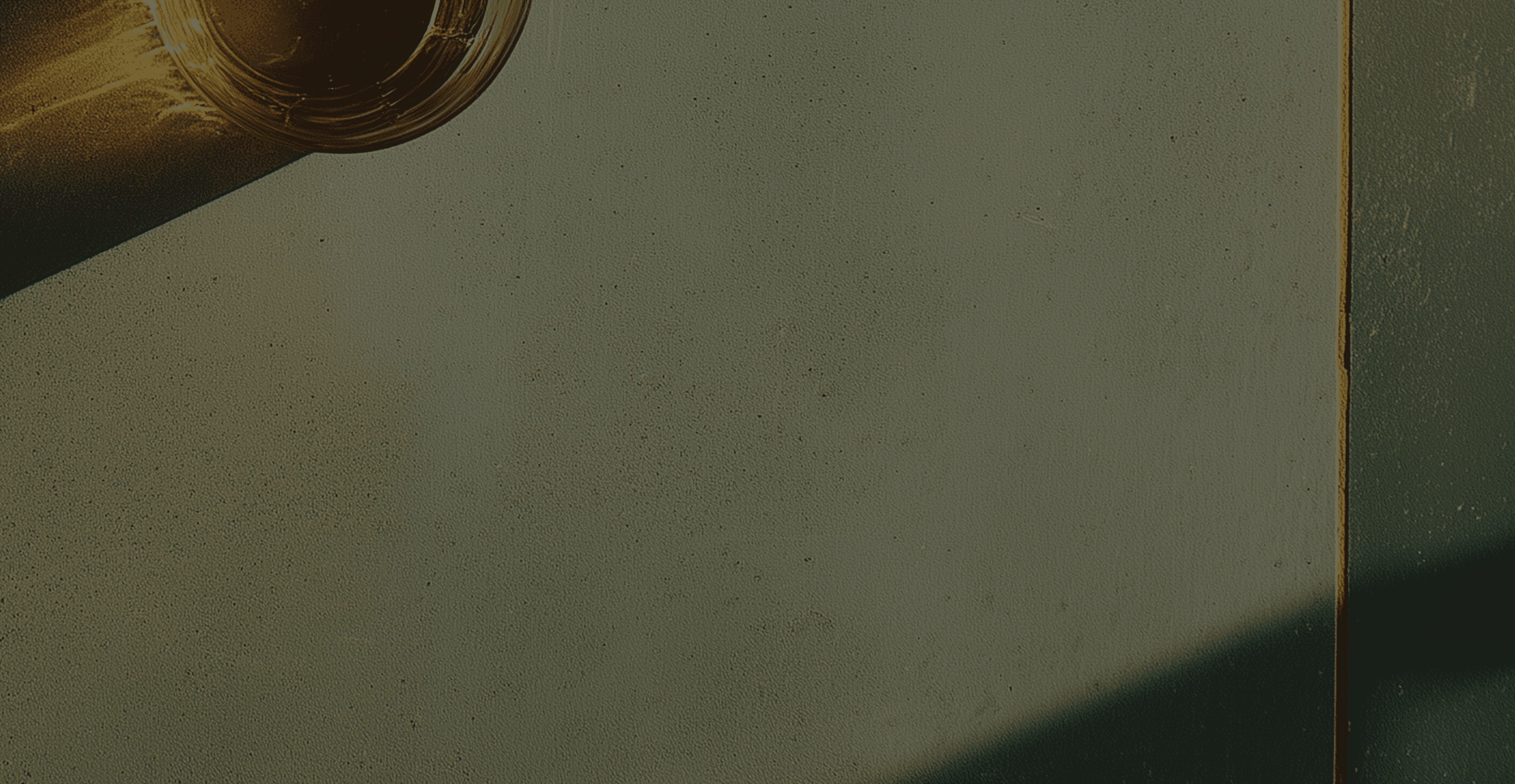 Top view of a glass filled with amber drink casting long golden shadows on a textured neutral surface in warm sunlight.