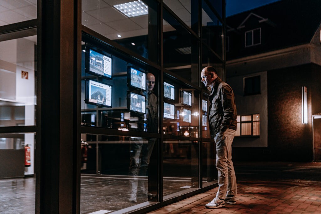 Man looking at property listings in a window at night.