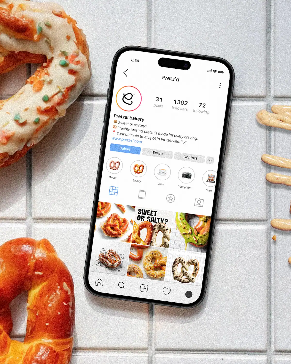 Mockup du profil Instagram Pretz'd sur smartphone posé sur carrelage, entouré de bretzels colorés et de sauce caramel.