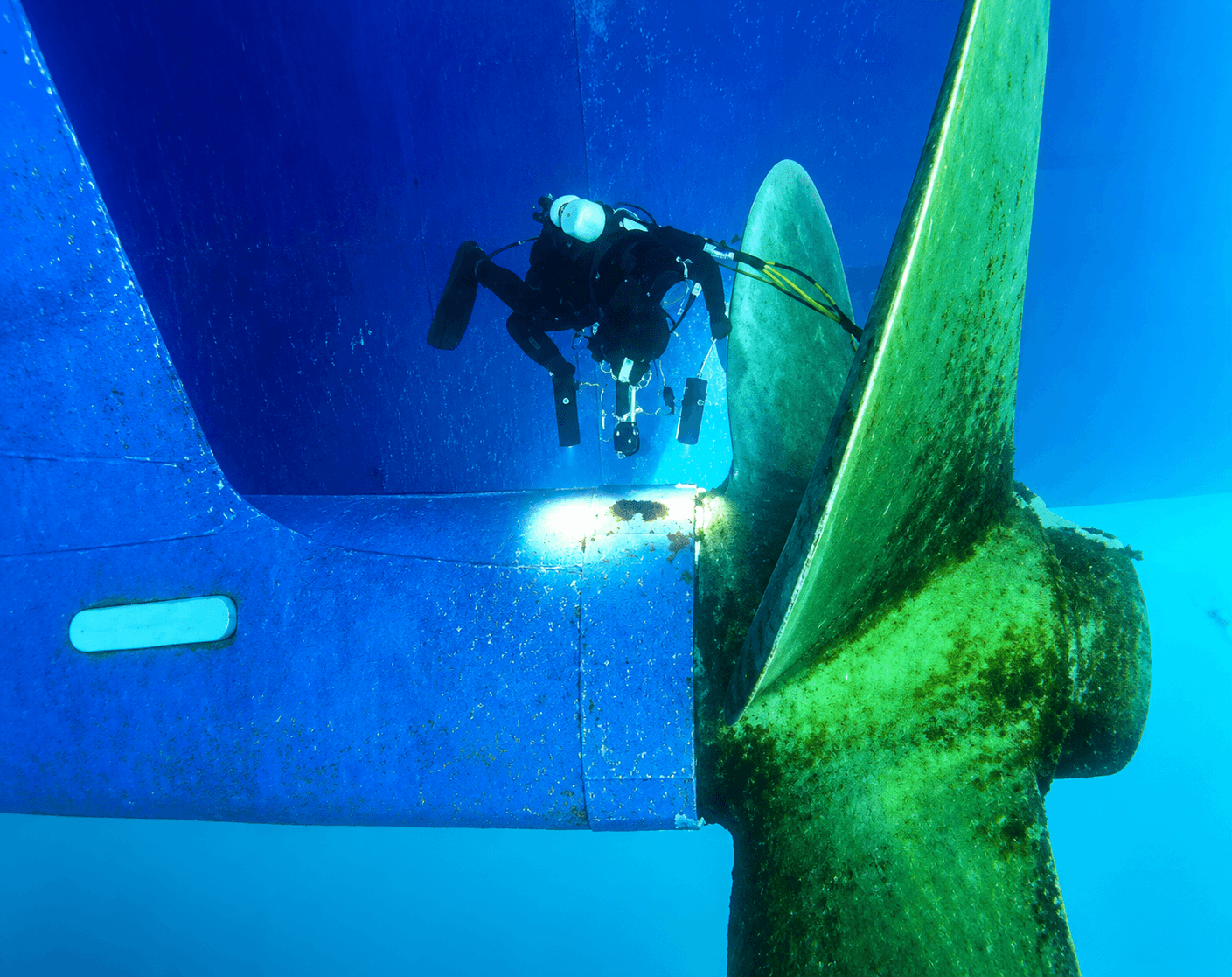 Illustrative underwater view of a diver examining a ship hull and propeller.