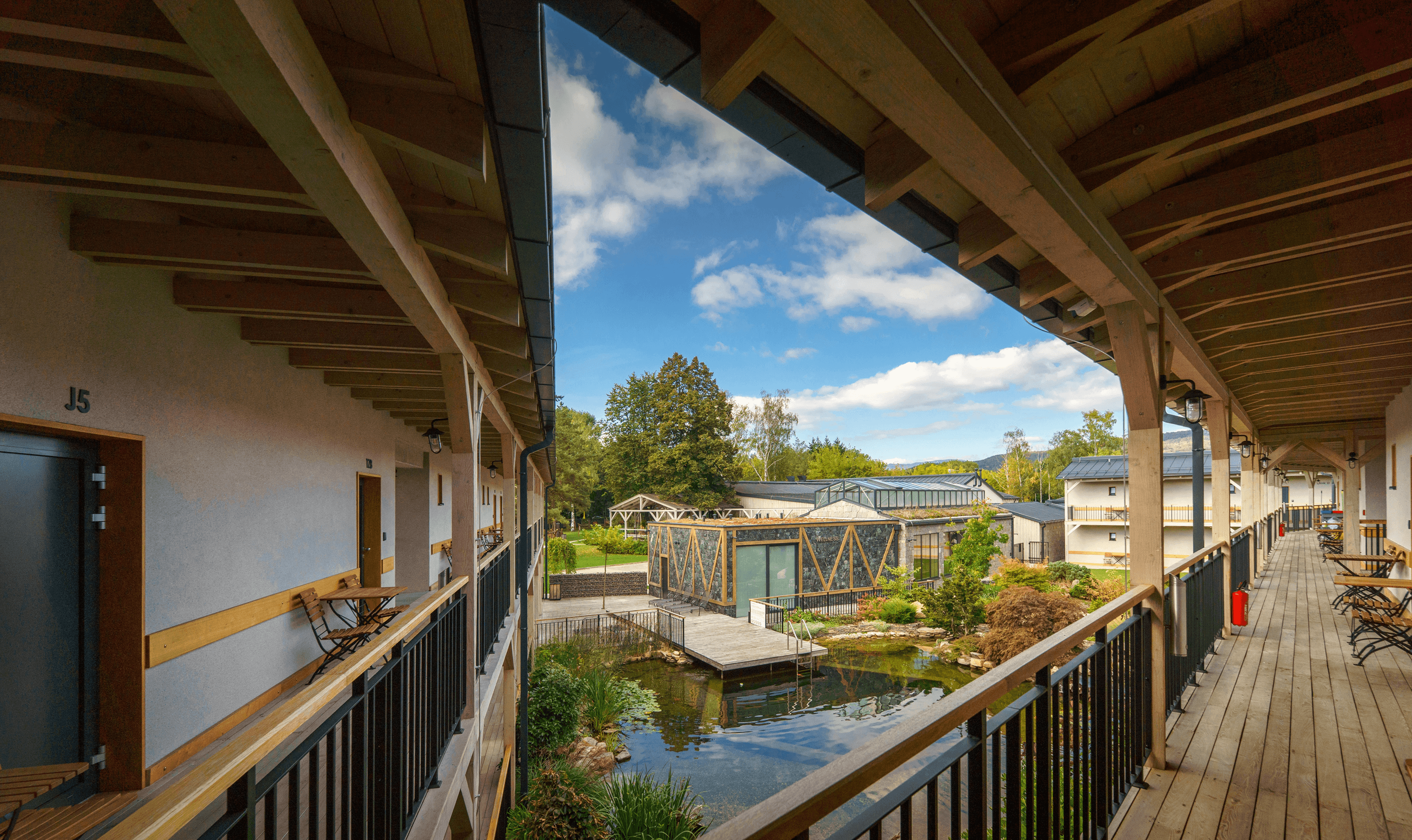 Balcony view of modern buildings and pond with trees and blue sky.