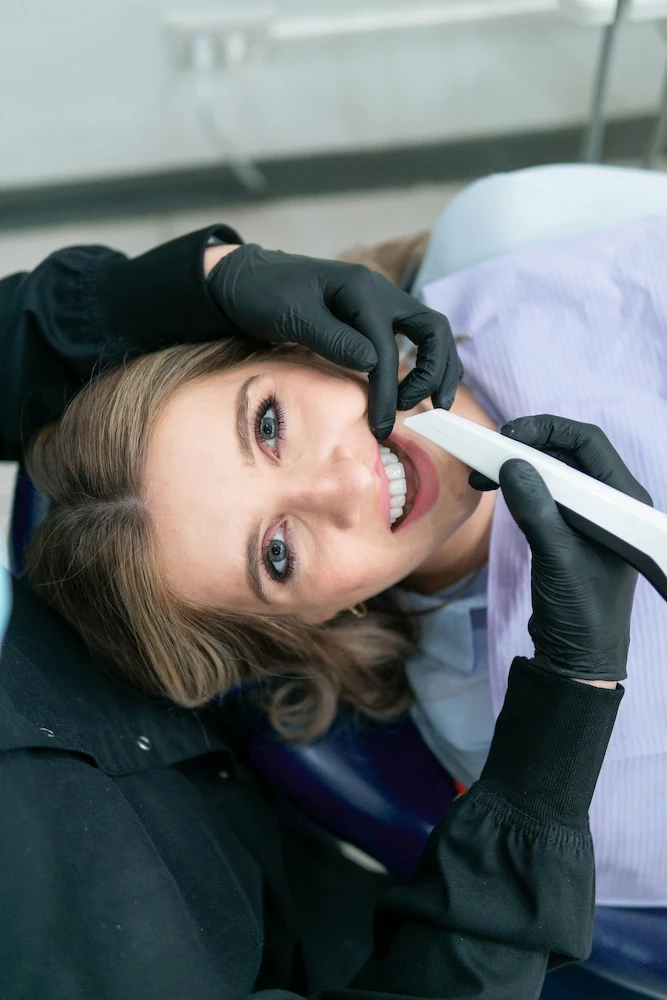 A female patient lies in a chair and a dentist holds an instrument near the patient's mouth.