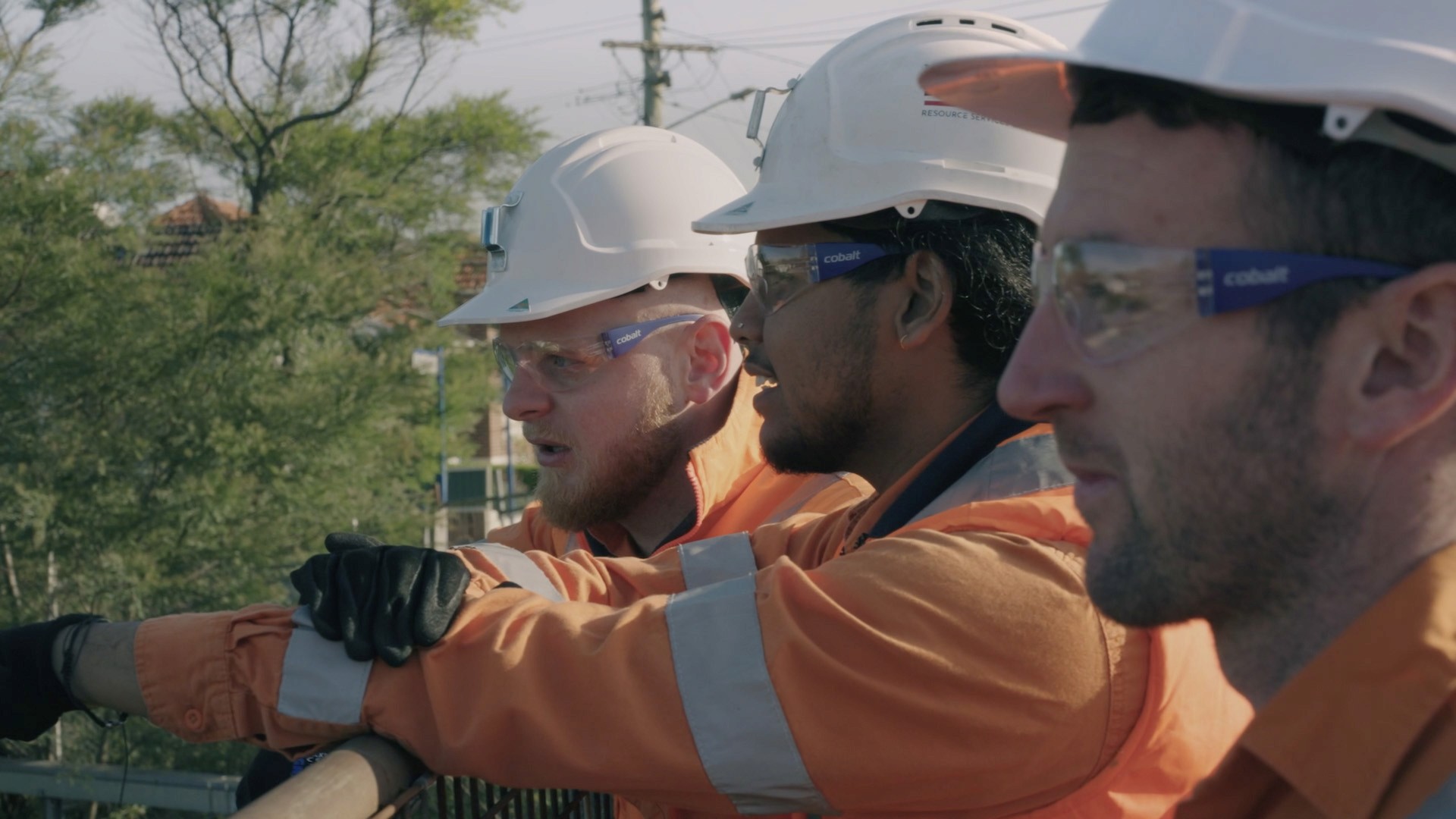 three men in safety helmets leaning over a railing