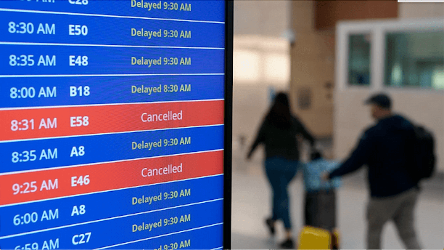 Travelers walk as a board shows delayed and canceled flights at Ronald Reagan Washington National Airport. Courtesy of The Hill.