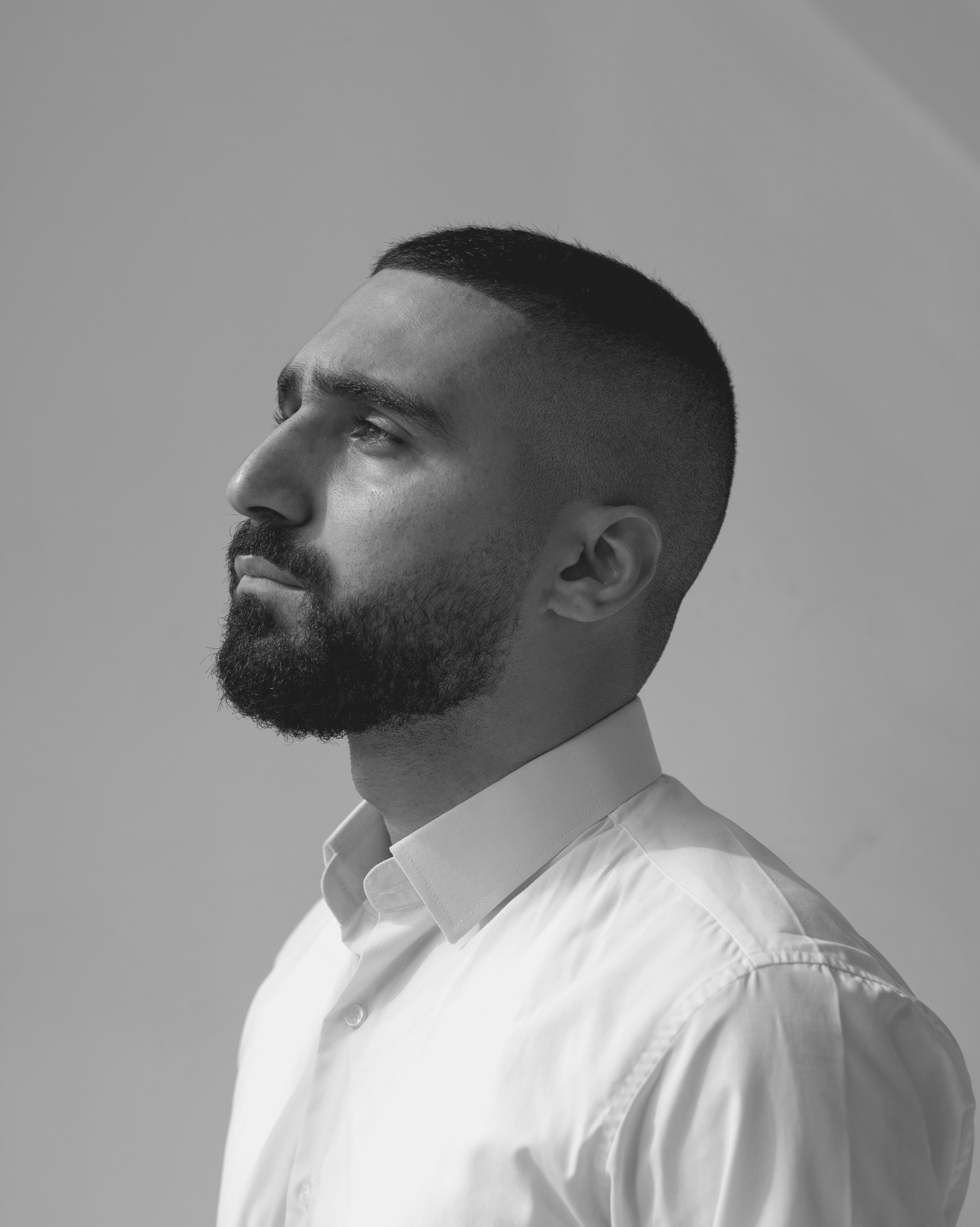 A thoughtful young person with dark hair gazes to the side, captured in soft black and white lighting.