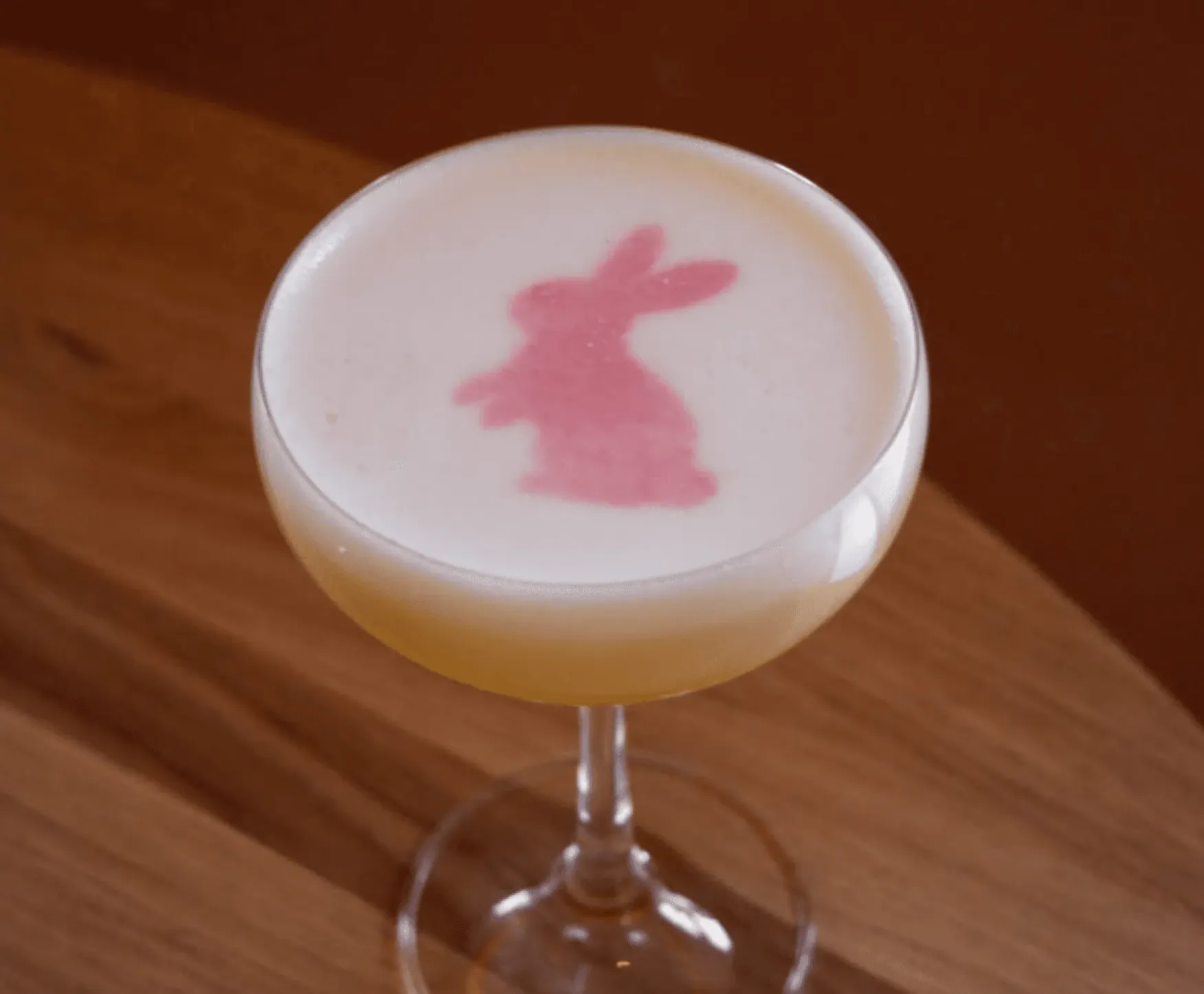 Close-up of an amber cocktail served over ice in a short glass, with a large orange peel garnish and a softly blurred bar setting in the background.