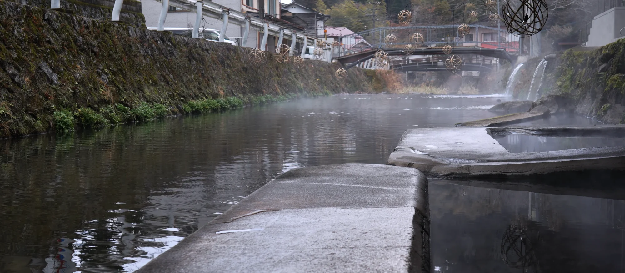 Steam rising off the river between stone embankments on a cold Kurokawa morning