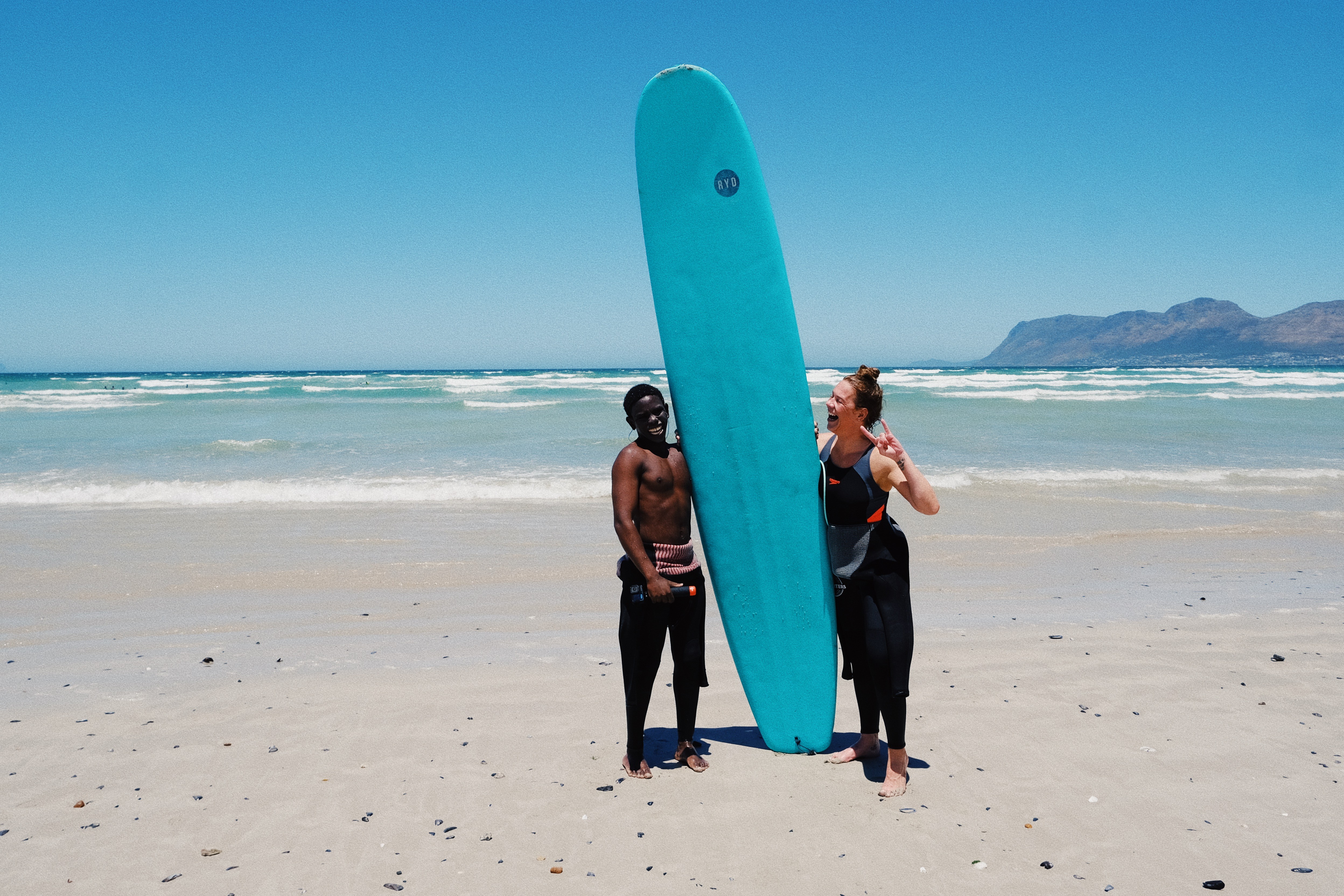 A surf coach with his surf student posing with the surfboard at Muizenberg beach in Cape Town