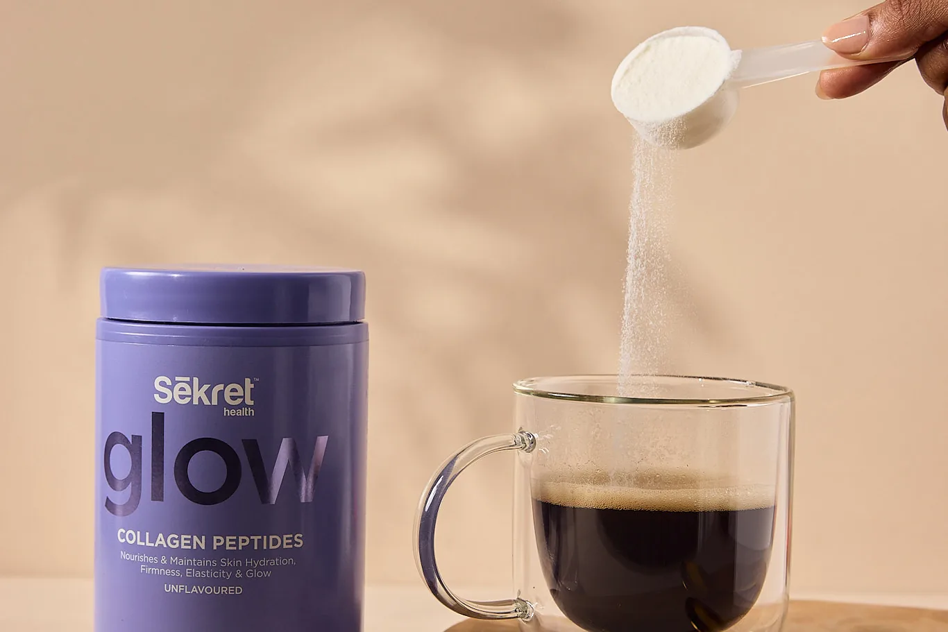A scoop of Sekret Glow collagen peptides poured into a glass of coffee beside the tub