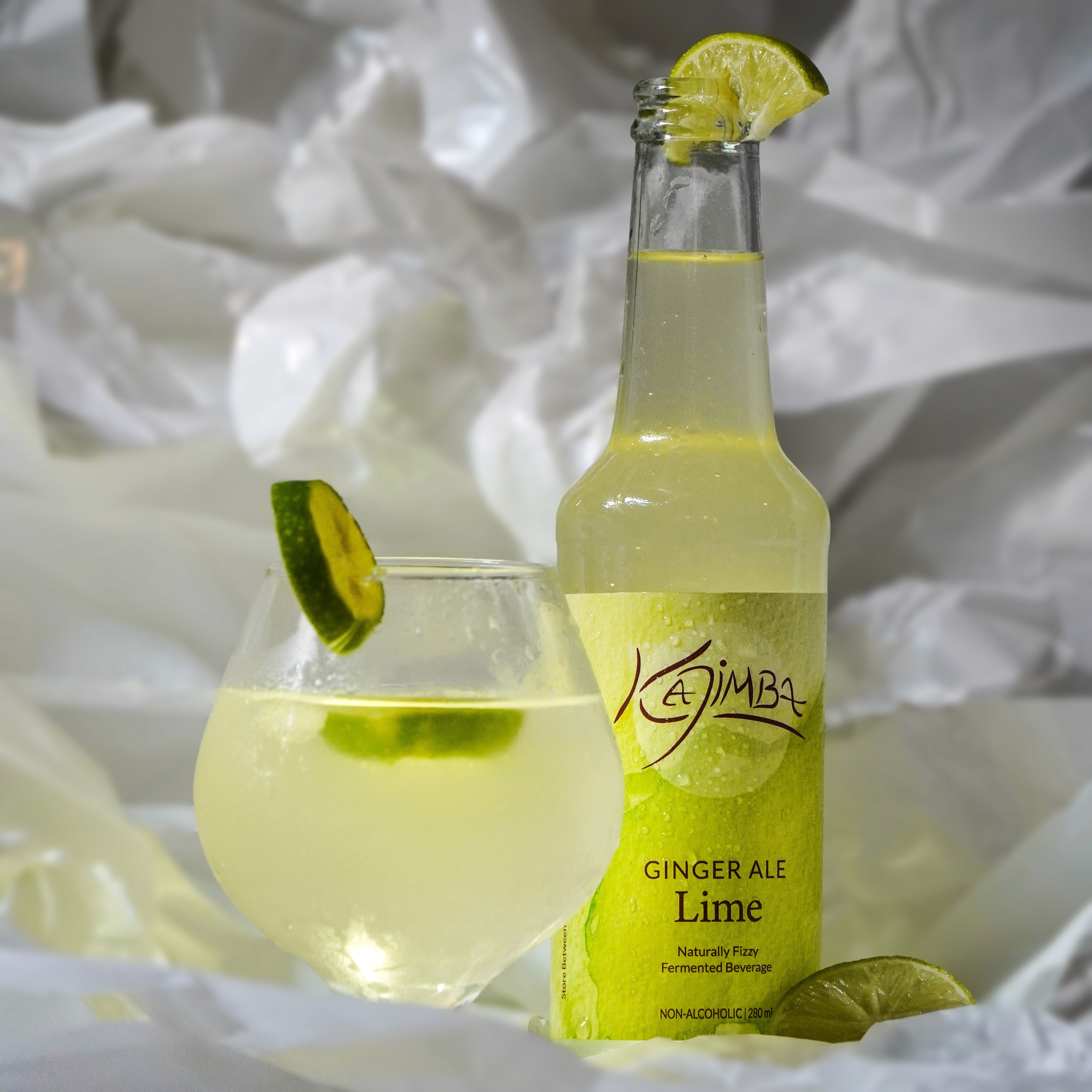 Lime Kajimba bottle next to a glass filled with Kajimba, both adorned with a lime slice.