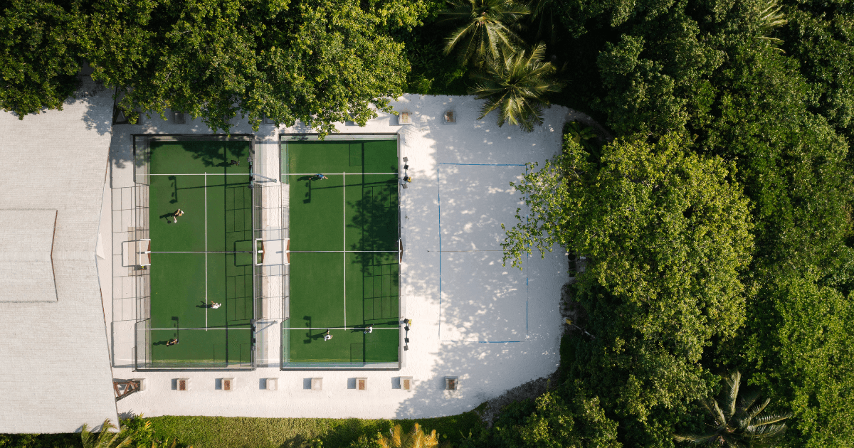 Aerial view of two green padel courts surrounded by lush tropical trees