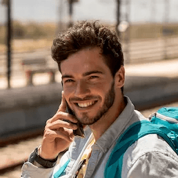 Homem com mochila em estação de trem falando ao telefone durante viagem