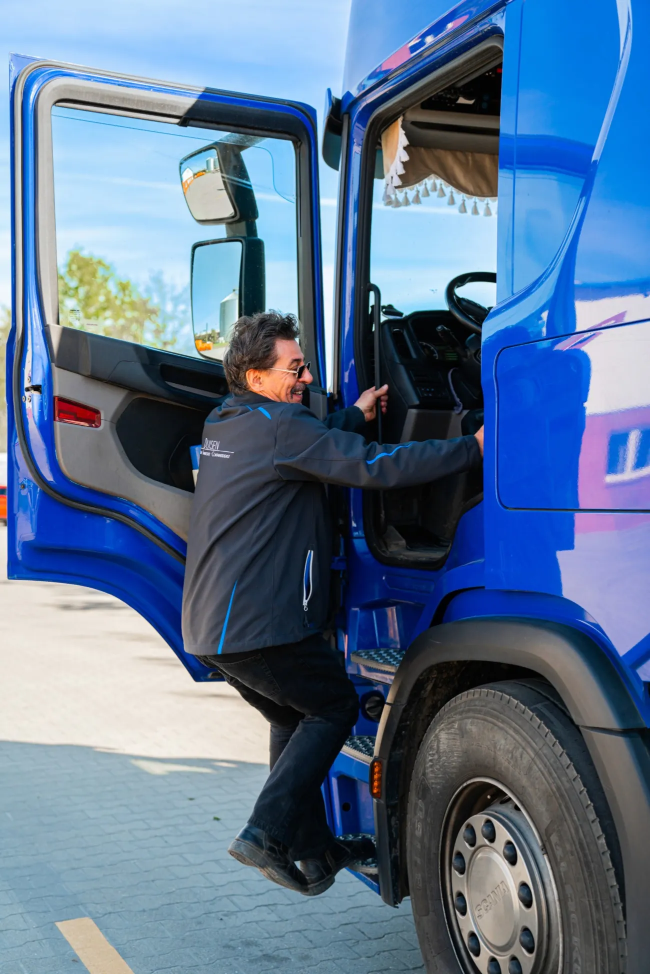Fahrer steigt lächelnd in die Kabine eines blauen Scania-Lkw
