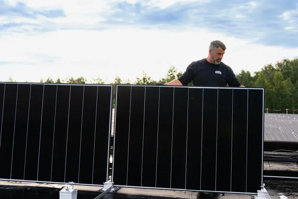 Mann installiert schwarze Solarmodule auf einem Dach für erneuerbare Energie.
