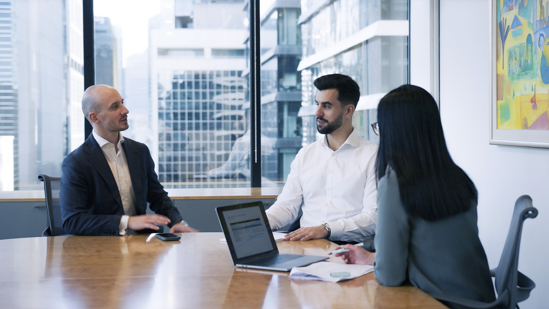 two men and a woman sitting around a boardroom table
