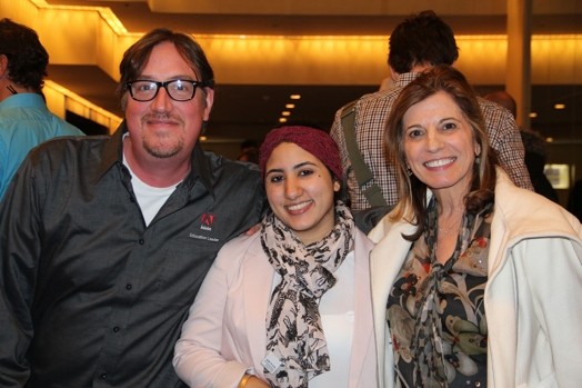 A photo of three people sitting among others at a conference.