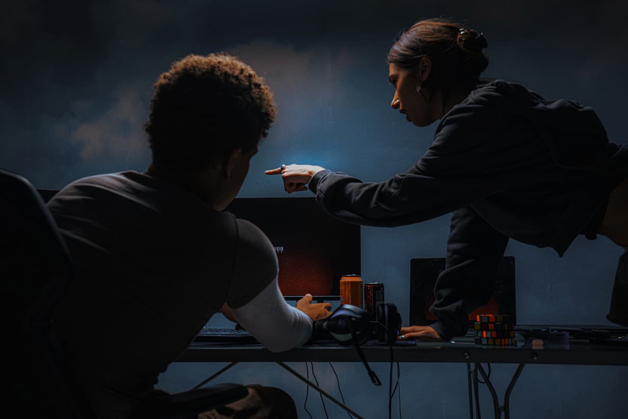 A man and woman facing and pointing at a computer.