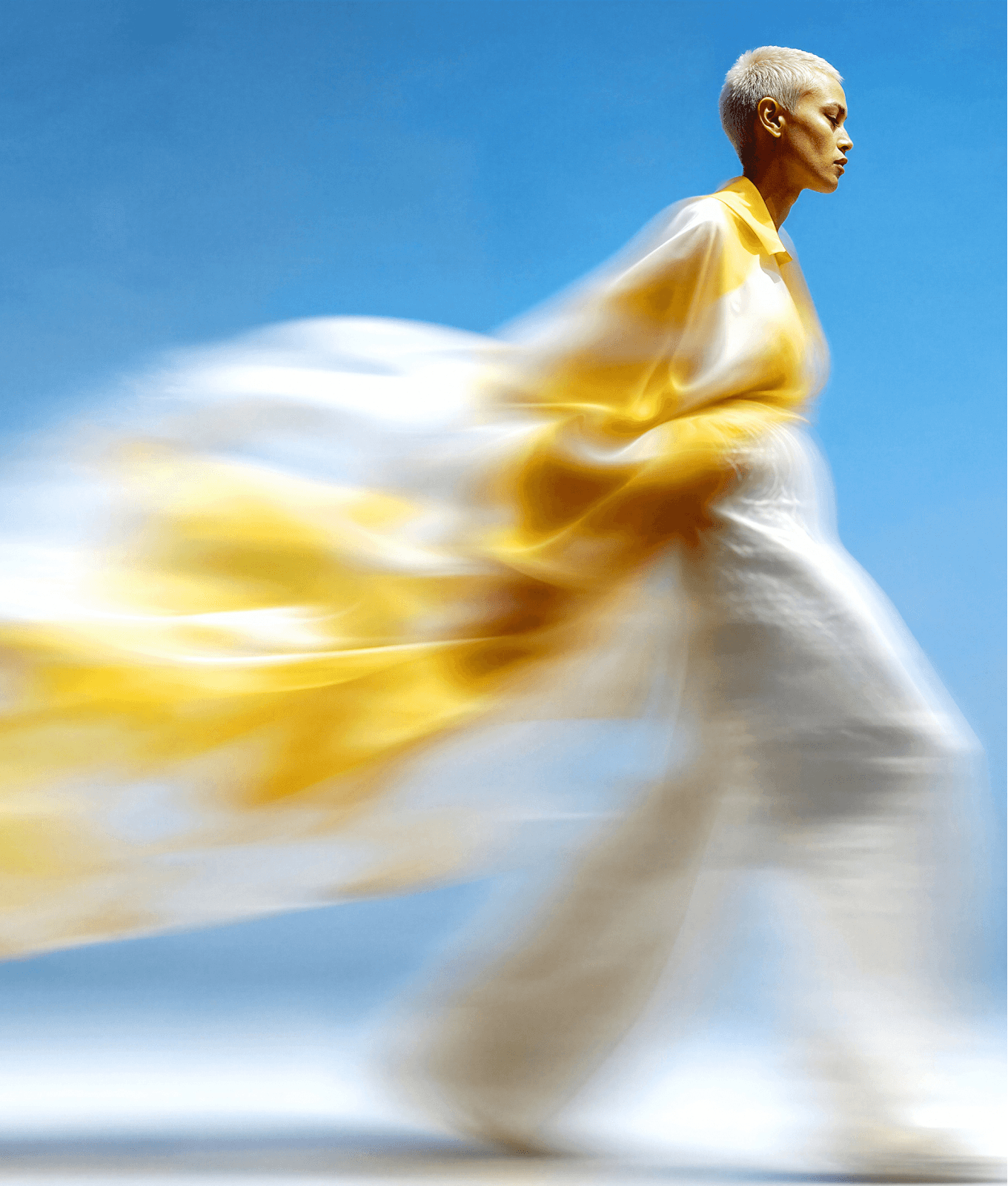 Homepage-Visual Design – Person in fliessendem Gelb-Weiss-Outfit in Bewegungsunschärfe vor sattblauem Hintergrund.
