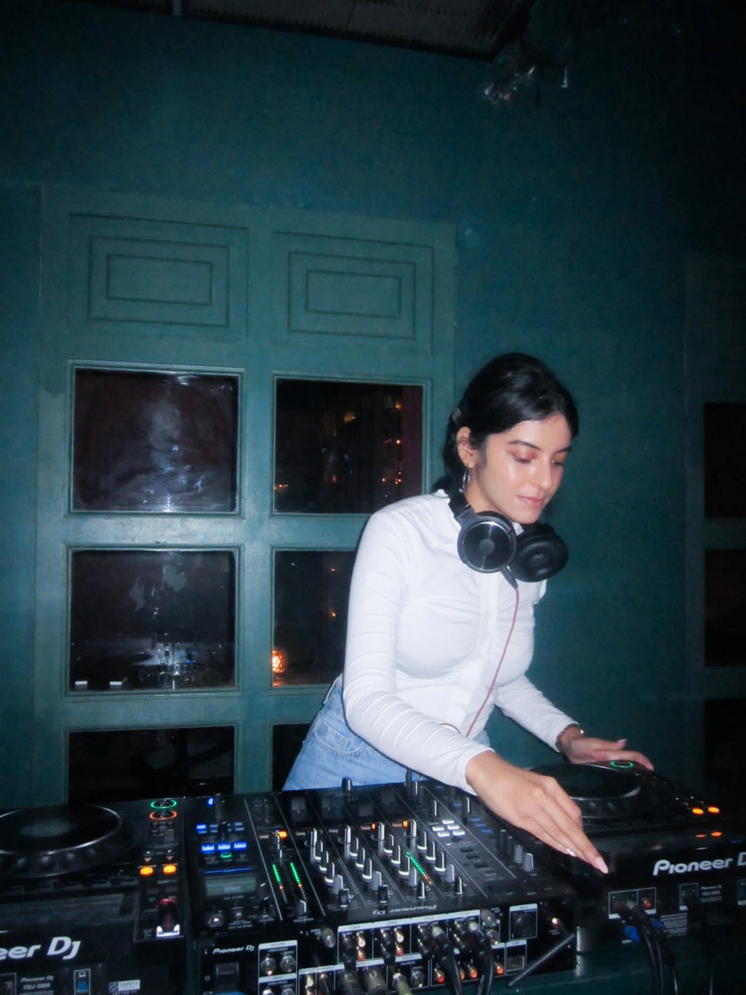 Green car under neon lights in a rainy city street