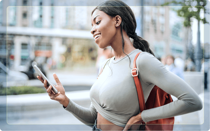 A young woman standing outdoors on a city street smiling while looking at her phone.