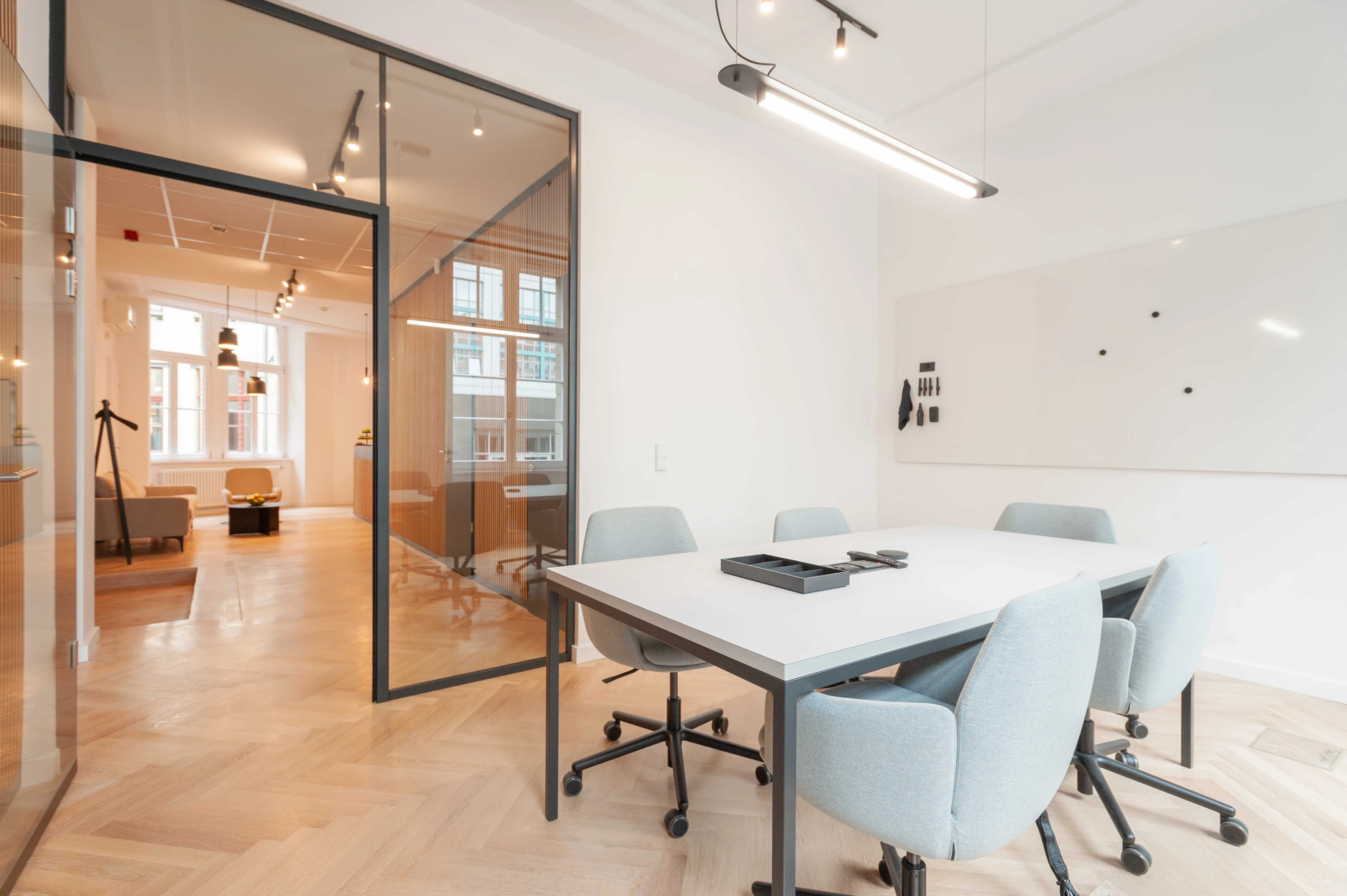Minimal white workstation at AI START-UP BERLIN with two monitors back to back on a white desk, black office chairs and slim black linear pendant lights.
