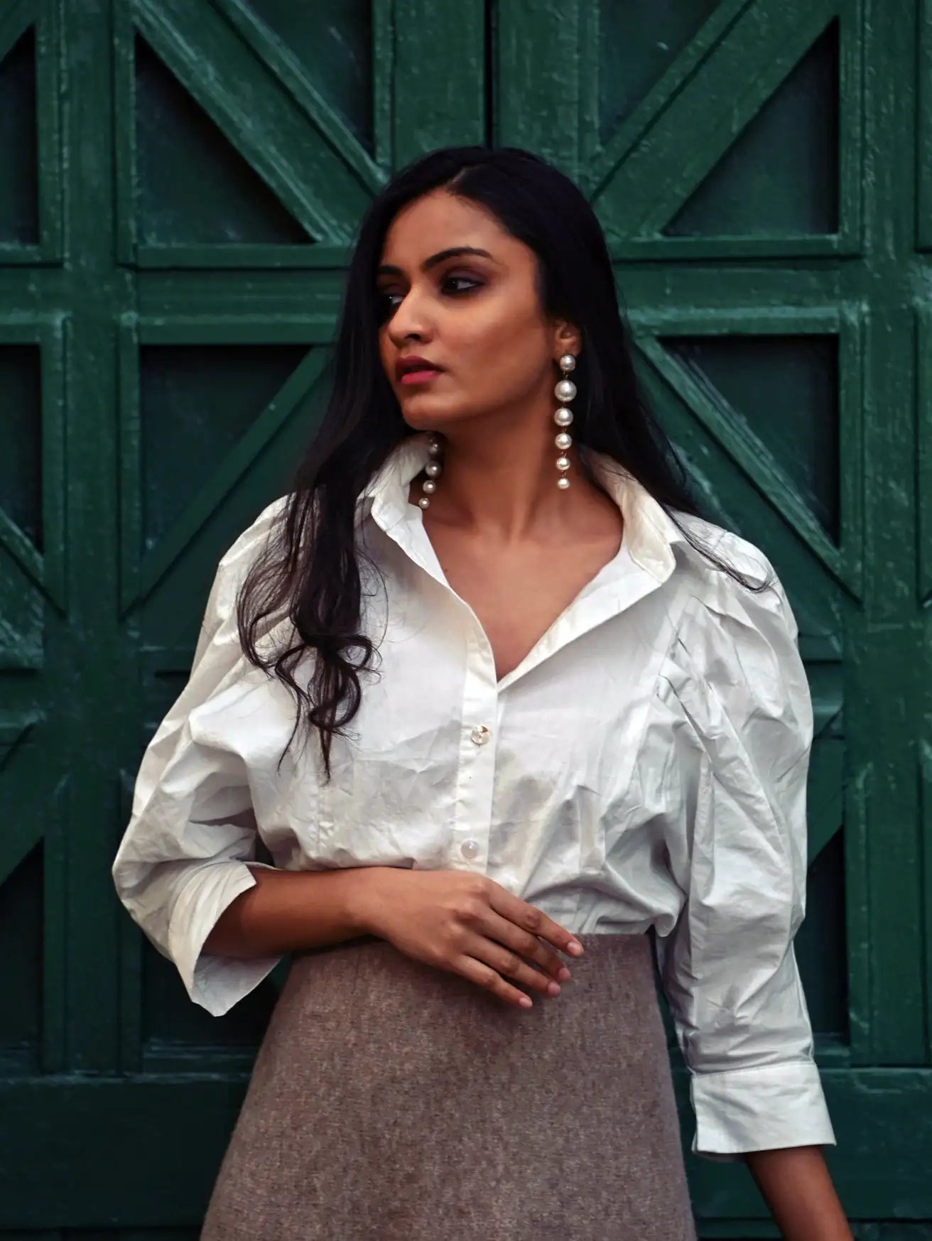 Woman in a crisp white puff-sleeve shirt and oatmeal skirt before a dark green wooden door