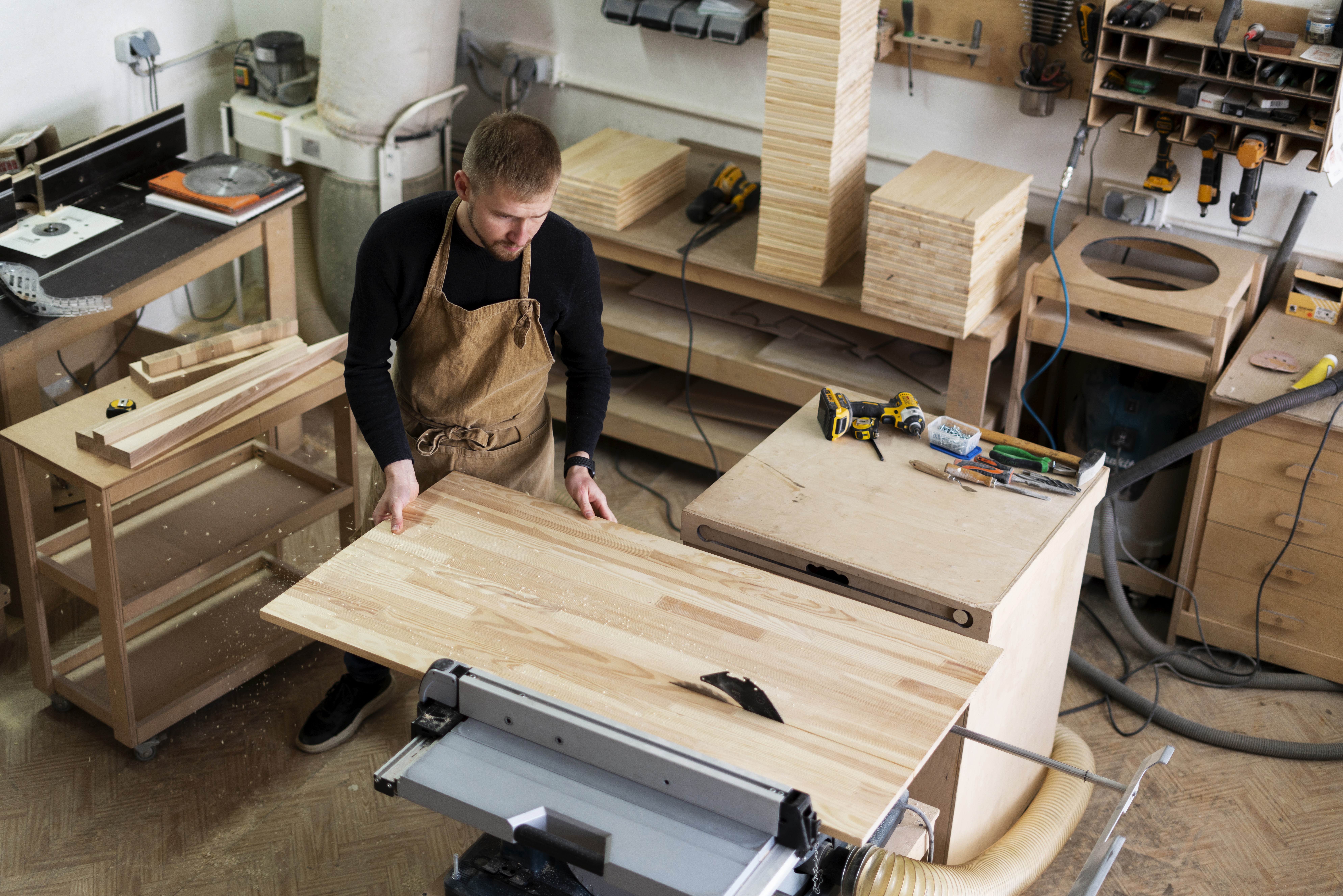Man assembling a white table with brown legs. The man is wearing a blue jumpsuit and leaning over the furniture.