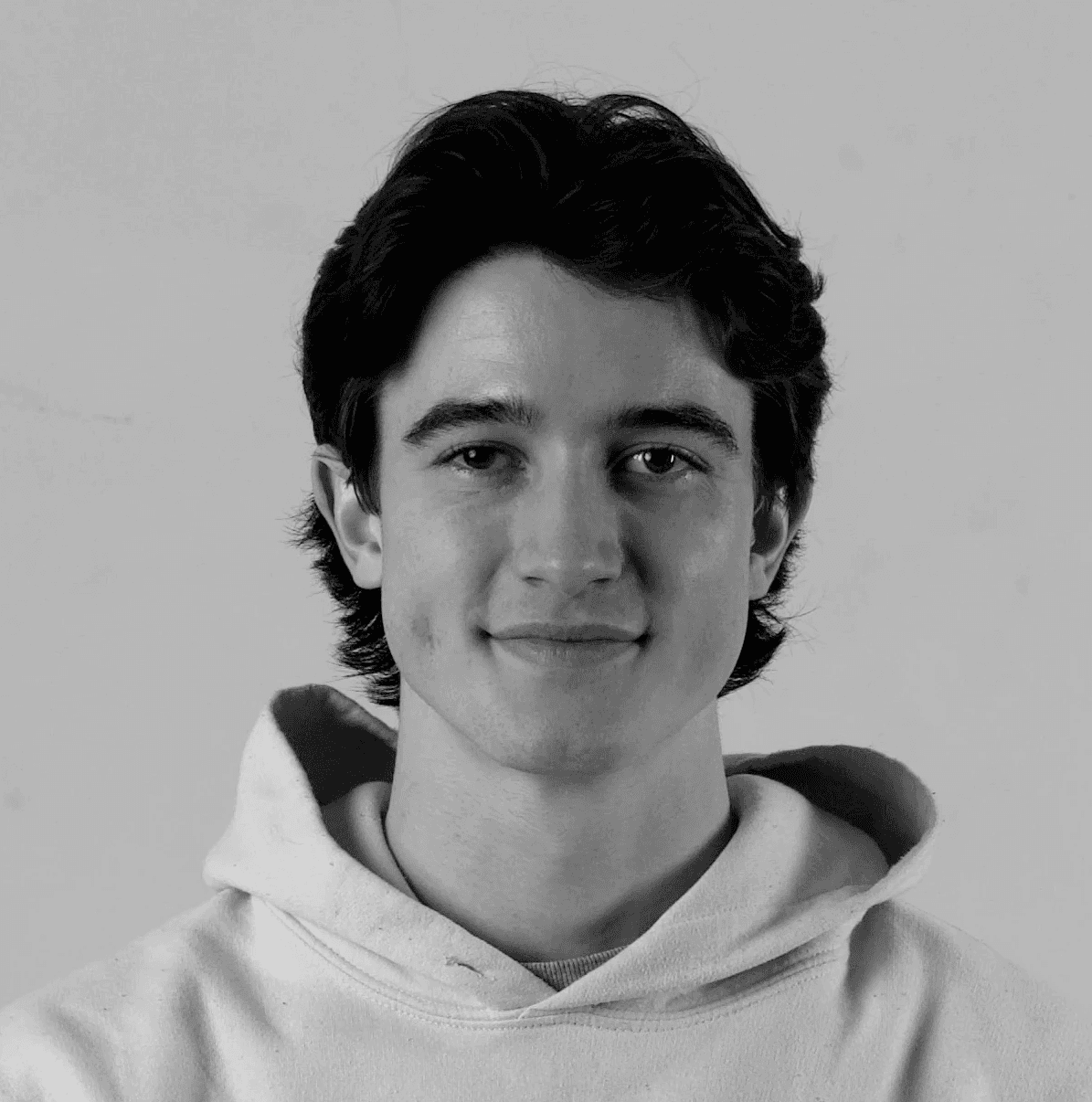 A thoughtful young person with dark hair gazes to the side, captured in soft black and white lighting.