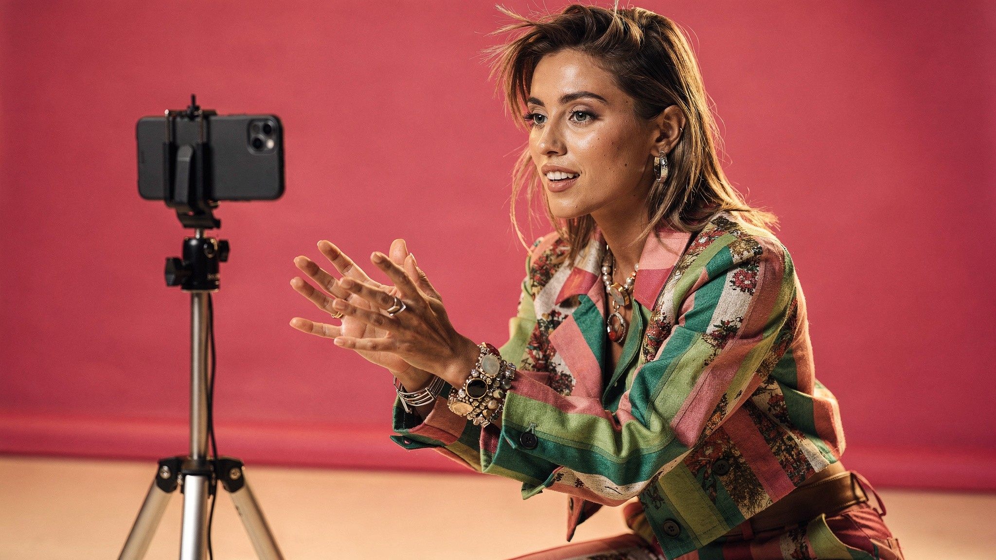 Adult content creator filming herself mid-gesture against a pink backdrop, phone on tripod, natural editorial light