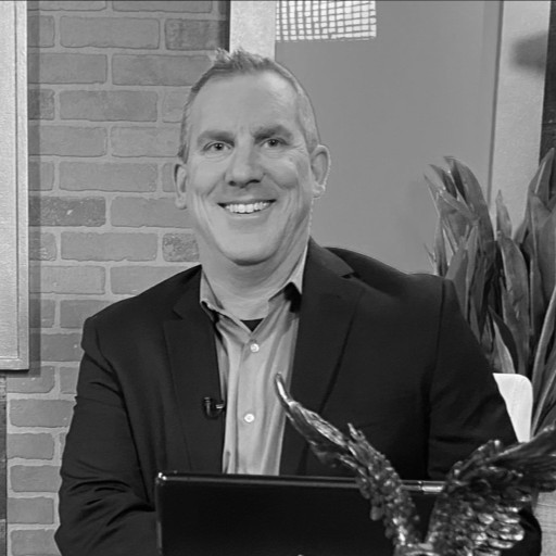 Stylish individual with curly hair and sunglasses against a bright blue sky, wearing a white tank top and a dark blazer.