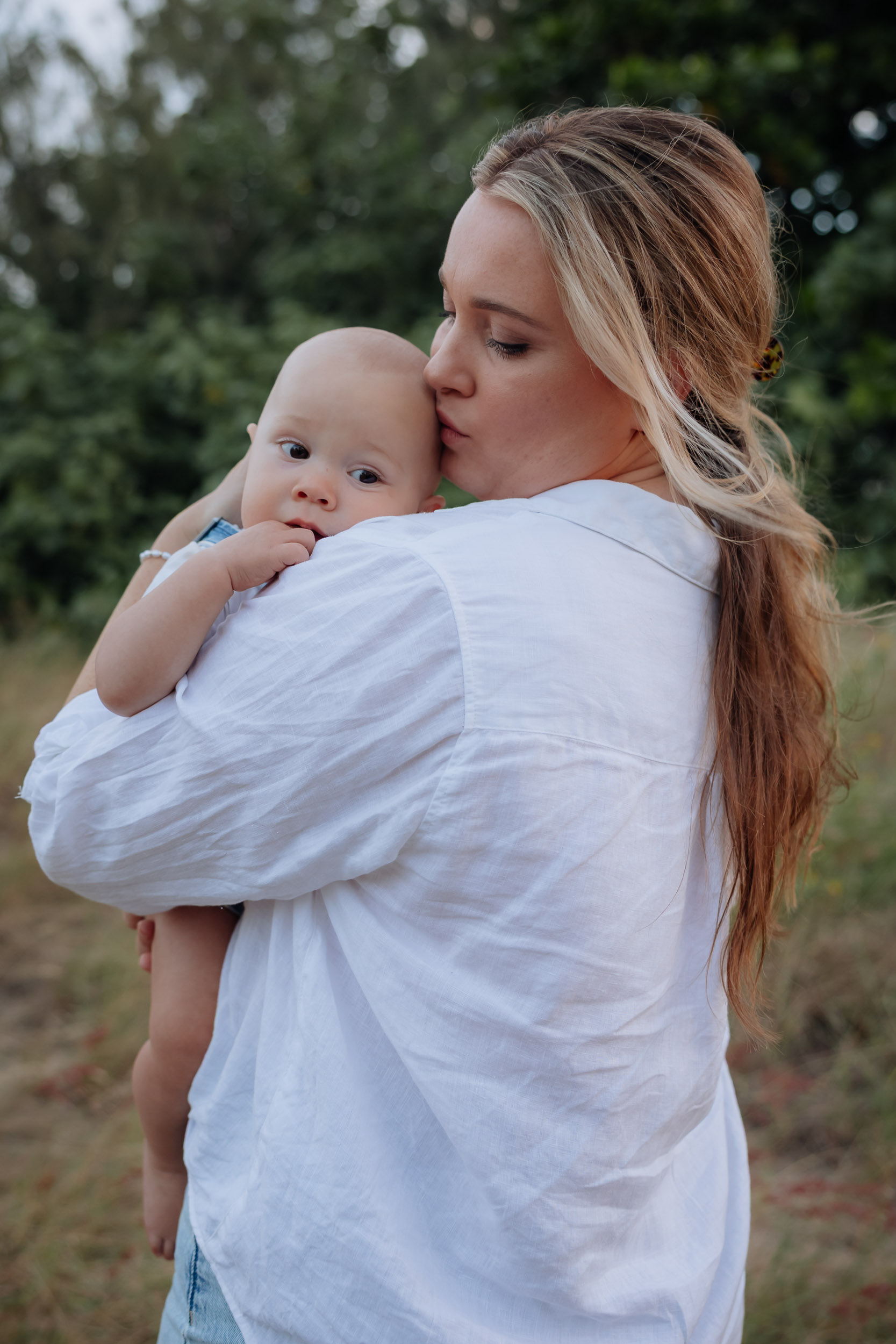 Mother and baby sharing a quiet moment in long green grass, outdoor motherhood photography Mackay